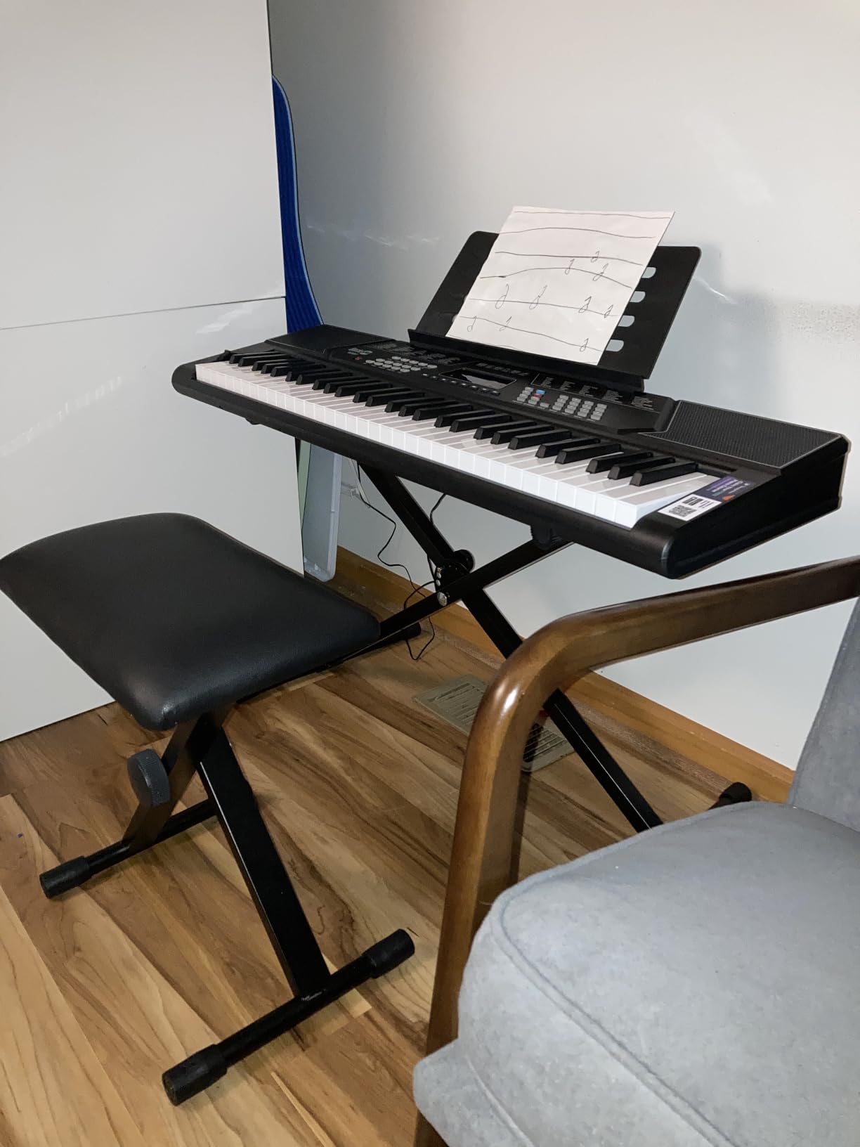 RockJam 61-key keyboard on its X-stand with the padded bench pulled up and hand-written notation on the music rest